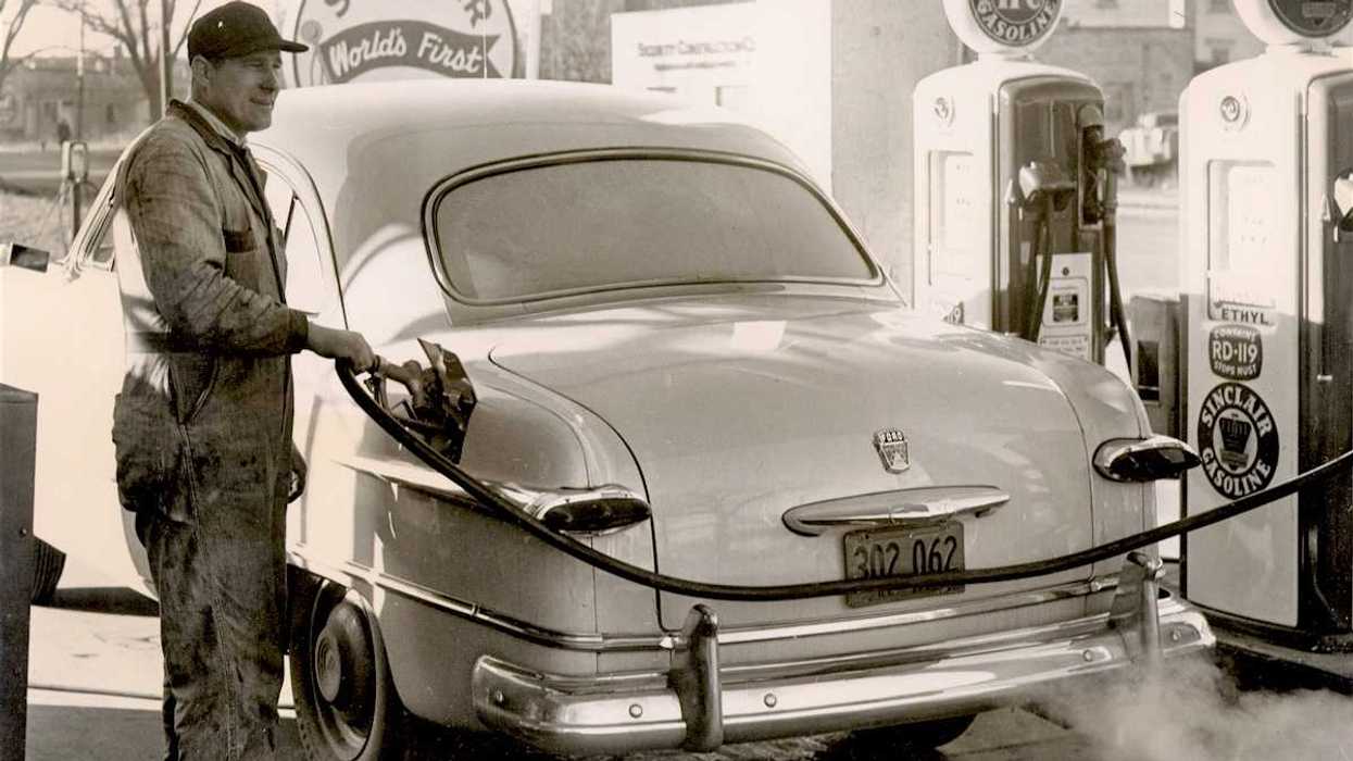 Black & white photo from 1950's of a gas station attendant pumping gas at a Sinclair station