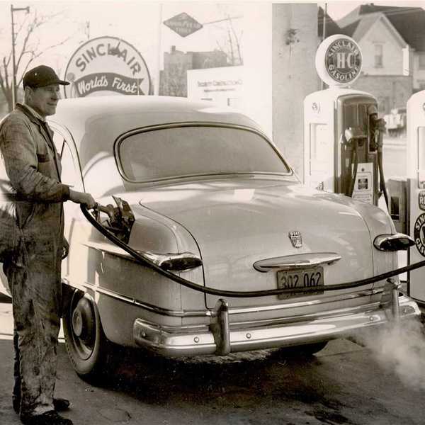 Black & white photo from 1950's of a gas station attendant pumping gas at a Sinclair station