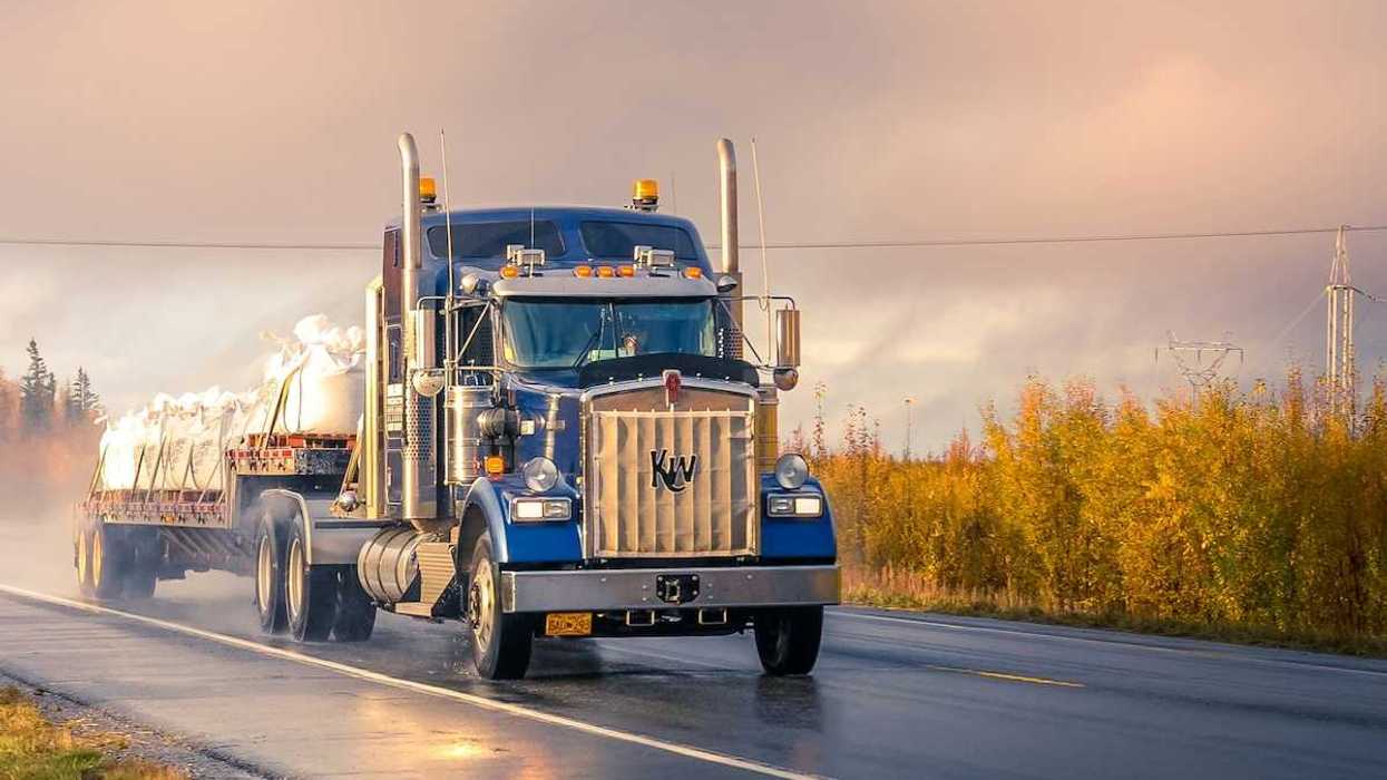 Blue semi truck pulling a flatbed trailer on a two lane highway