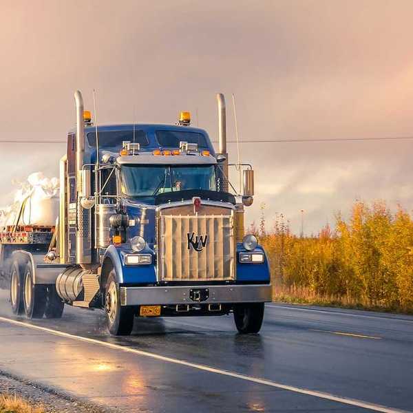 Blue semi truck pulling a flatbed trailer on a two lane highway