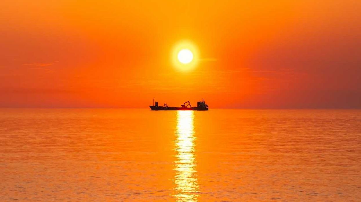 Boat on the ocean highlighted against an orange, burning sun