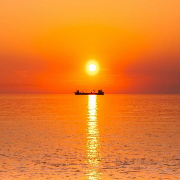 Boat on the ocean highlighted against an orange, burning sun