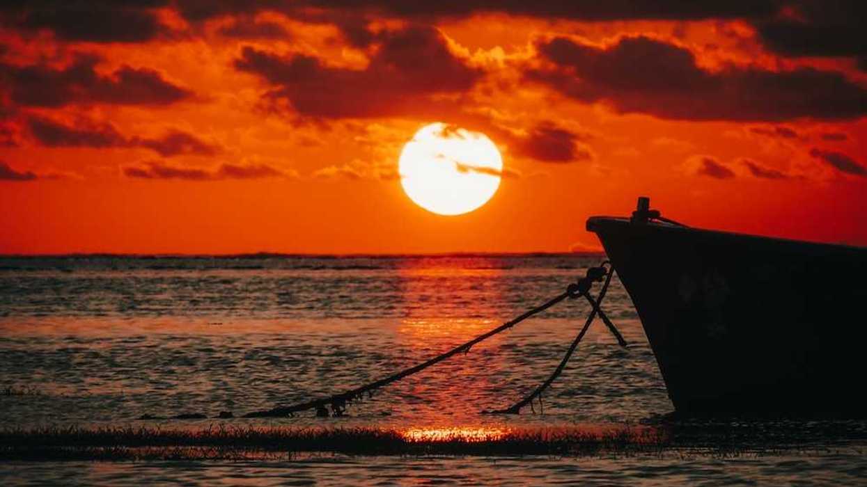 Bow of a moored boat against a brilliant red-orange sunset over the ocean