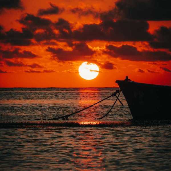Bow of a moored boat against a brilliant red-orange sunset over the ocean