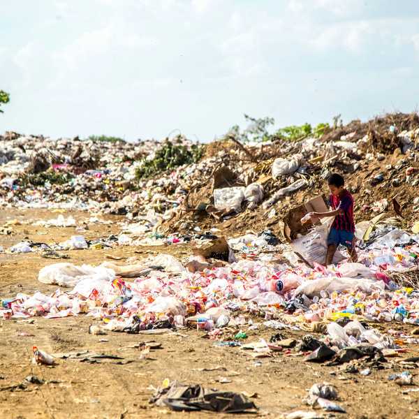 Boy walking through a landfill covered in plastic waste.