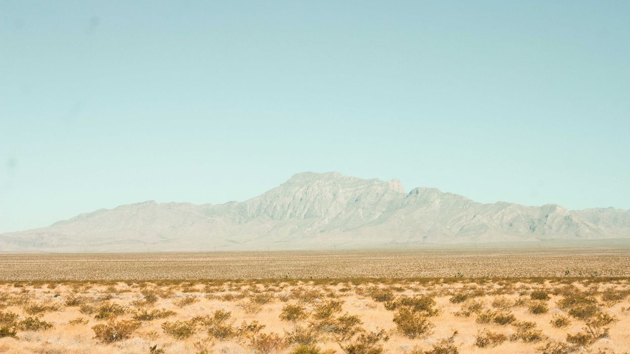 brown field near mountain under blue sky during daytime
