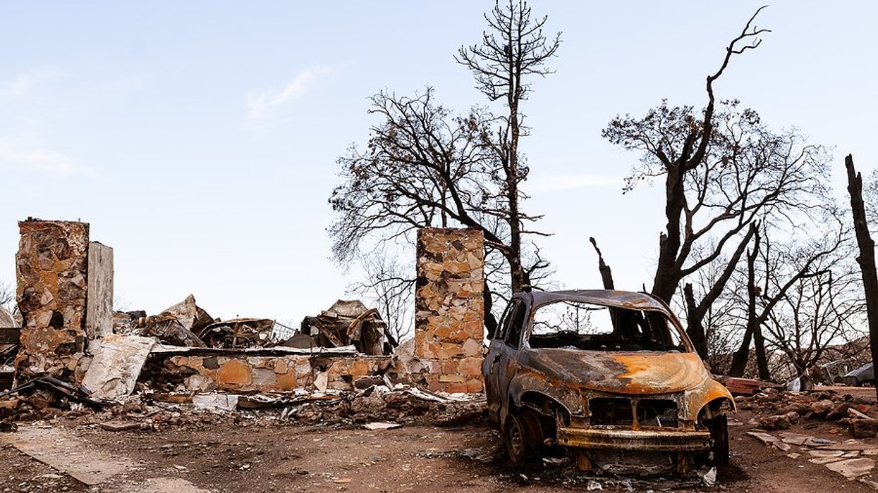 Burned foundation of a home next to burned out car and trees.