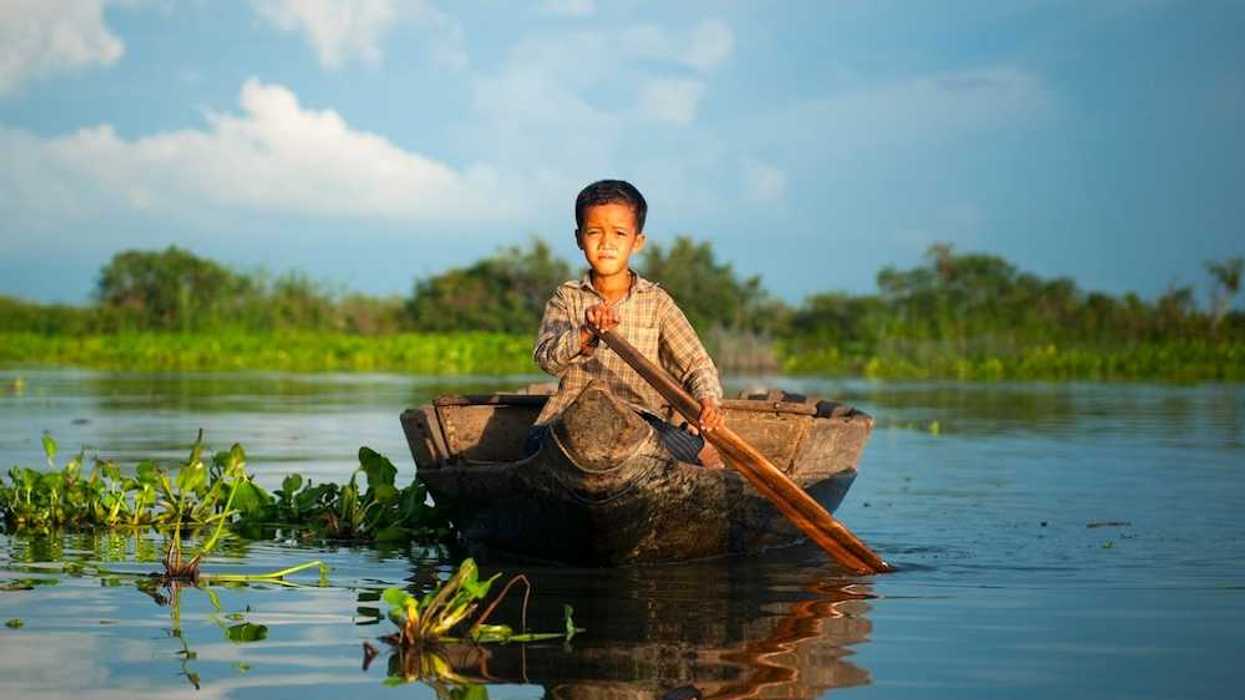 Cambodian boy in plaid shirt paddling a dugout canoe on a Cambodian river