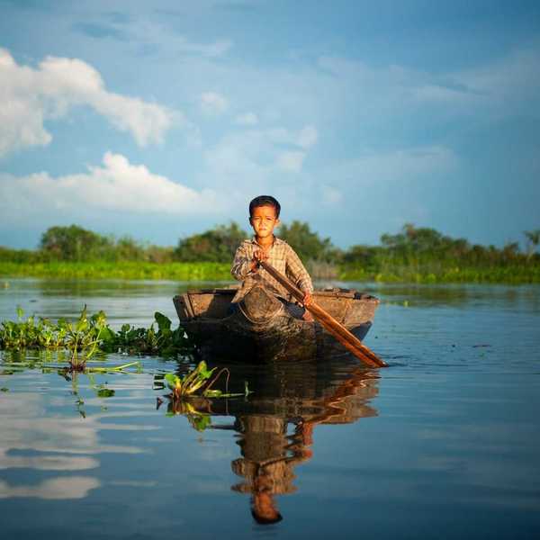 Cambodian boy in plaid shirt paddling a dugout canoe on a Cambodian river