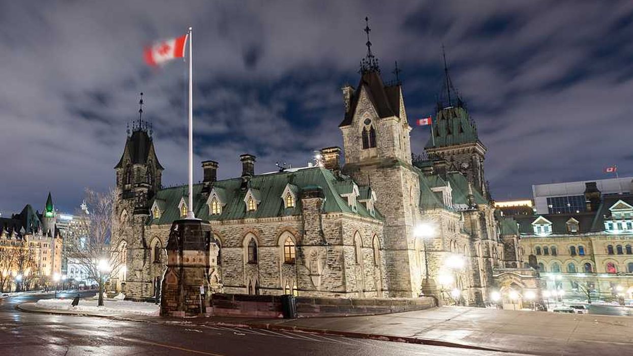 Canadian parliament building with a Canadian flag waving above it on a dark night