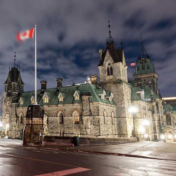 Canadian parliament building with a Canadian flag waving above it on a dark night