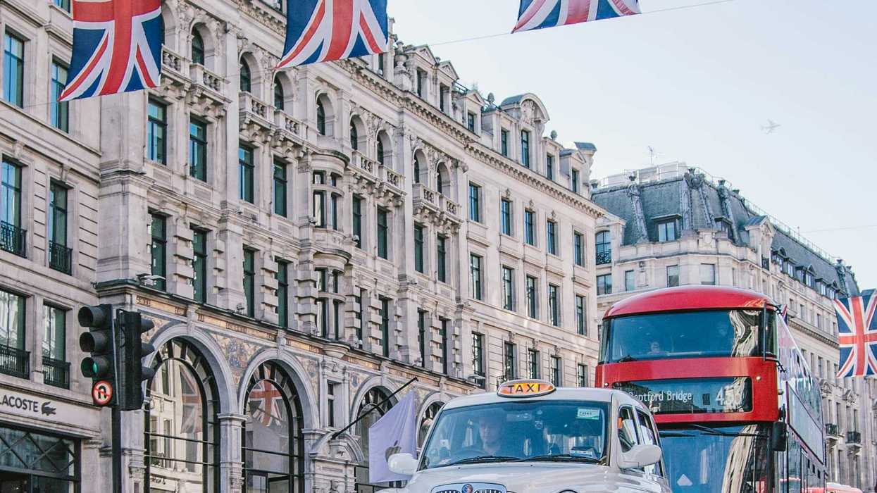 Cars and buses driving on Oxford Street in London with British flags strung across the street.