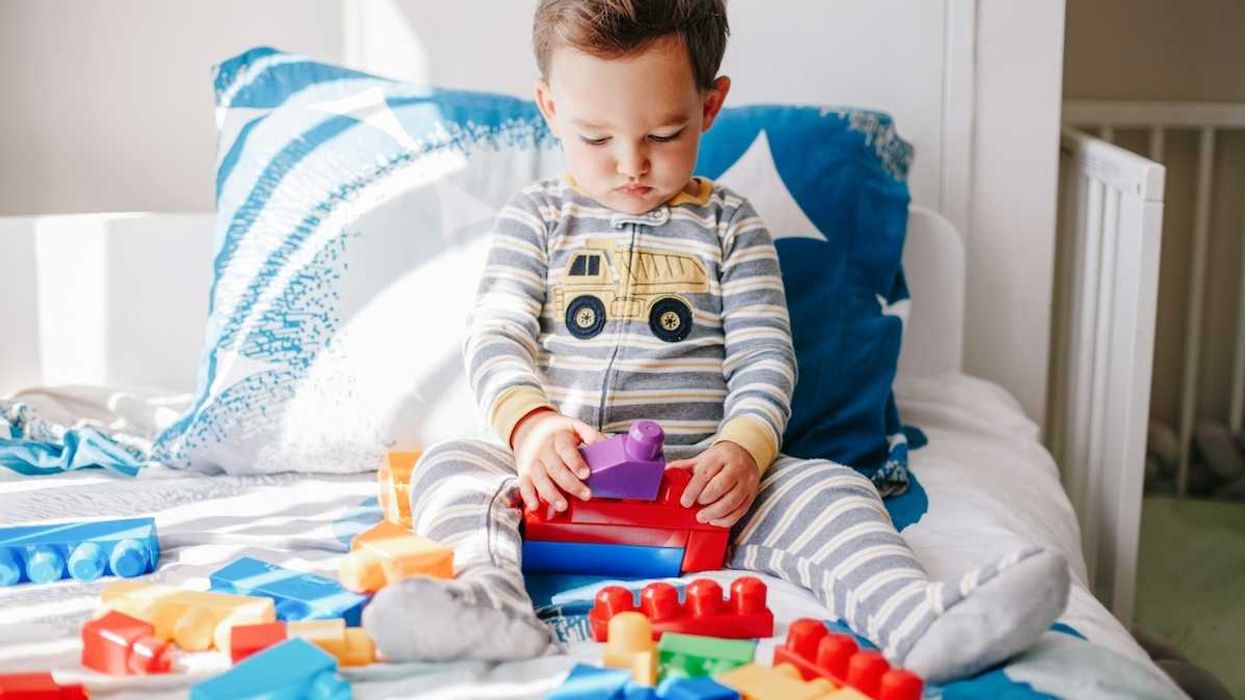Child in pajamas playing with plastic toys on bed