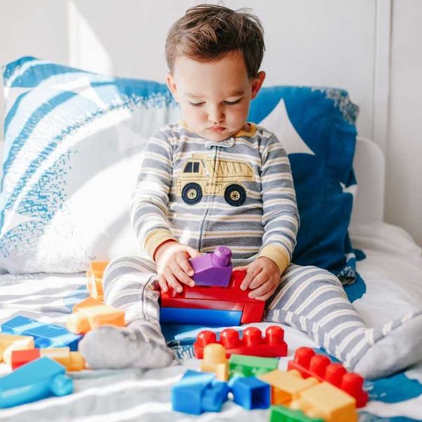 Child in pajamas playing with plastic toys on bed