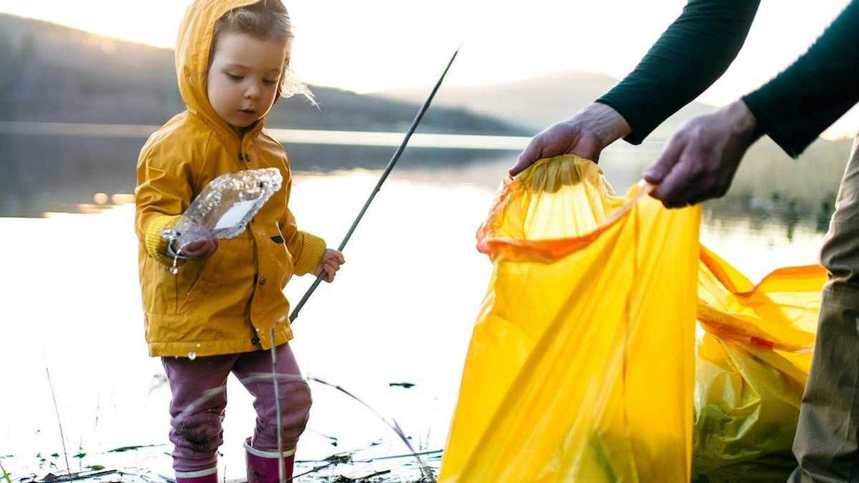 Child in yellow plastic raincoat picking up litter on edge of waterbody