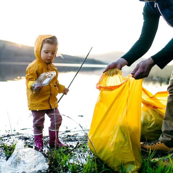 Child in yellow plastic raincoat picking up litter on edge of waterbody