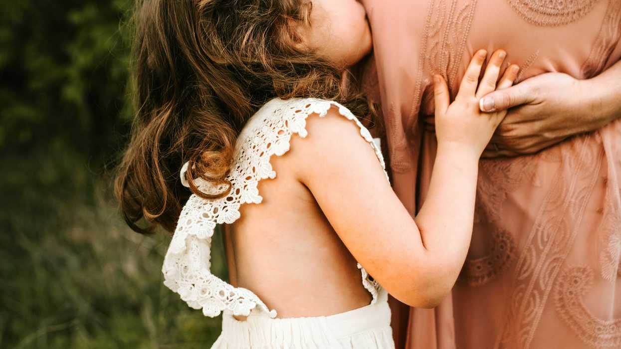 child kissing woman's pregnant tummy.