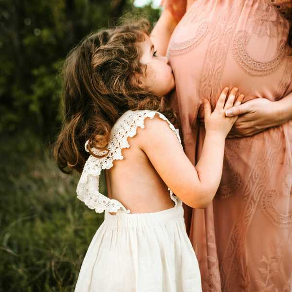 child kissing woman's pregnant tummy.
