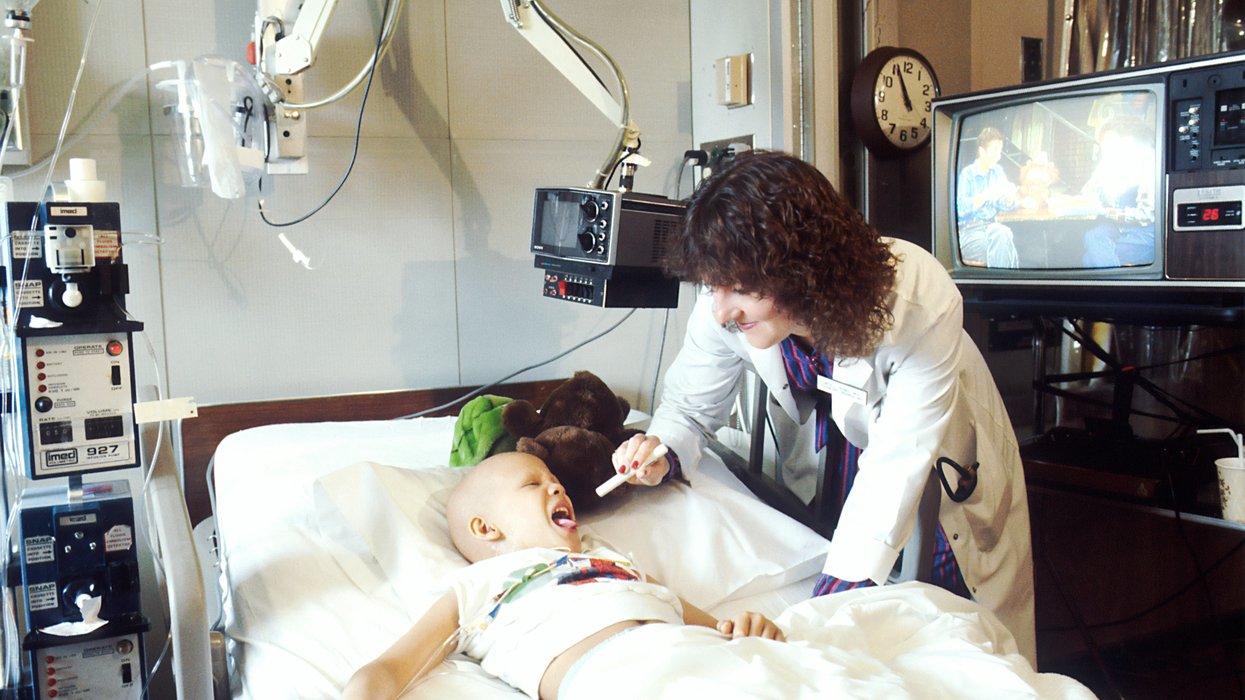 Child lying on hospital bed with doctor checking their mouth.