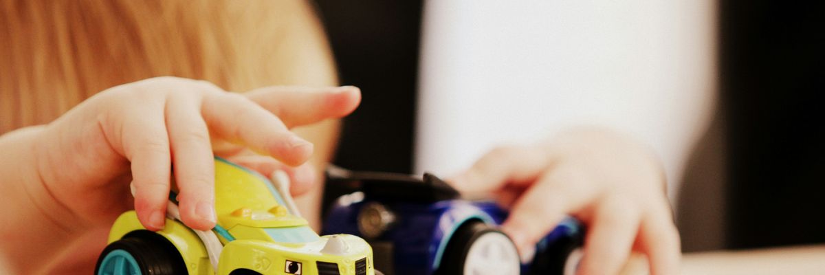 child playing with two green and blue car plastic toys on a table.