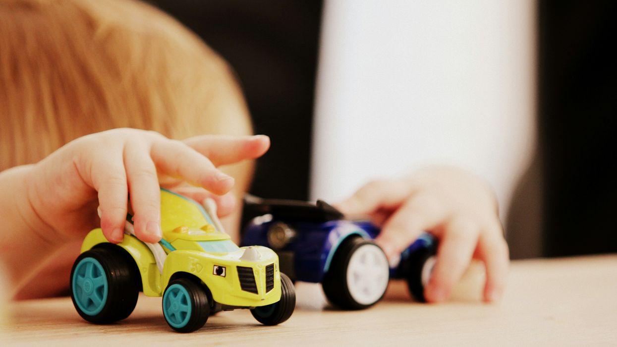child playing with two green and blue car plastic toys on a table.