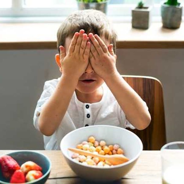 Child sitting at a table in front of a bowl of cereal
