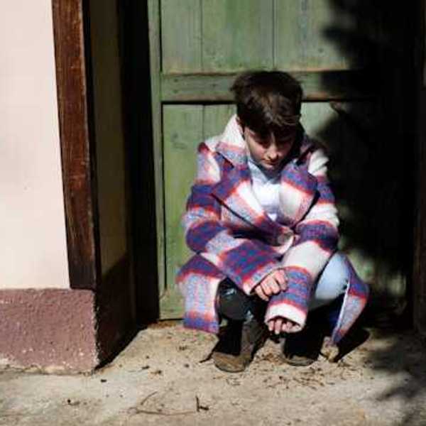 Child sitting in a doorway and looking down at the ground