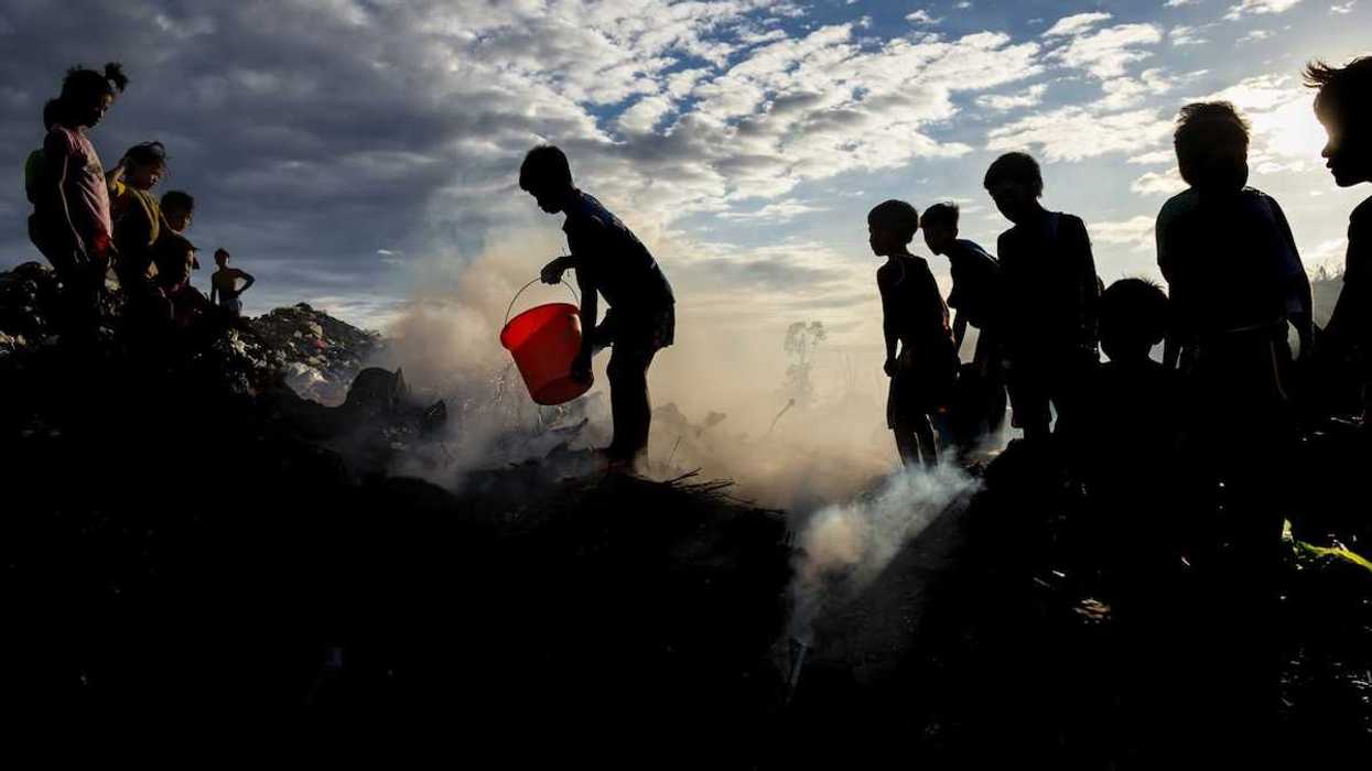 Child trash pickers on top of a smoking, smoldering, trash mountain.