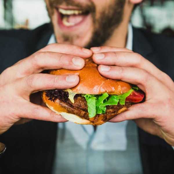 Closeup of man with a two-handed grip on a hamburger in a bun, mouth open, about to eat.