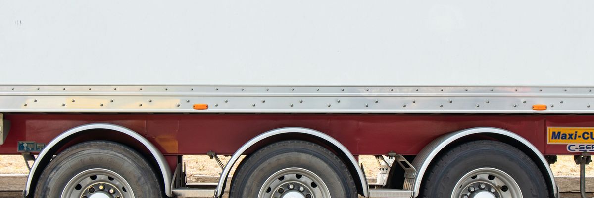 Closeup of the side of a flatbed truck showing three tires on one side.