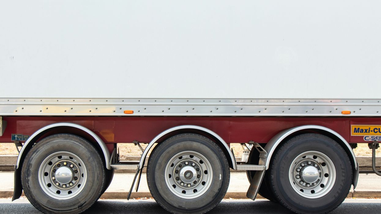 Closeup of the side of a flatbed truck showing three tires on one side.