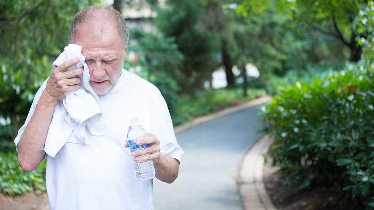 Closeup portrait old gentleman in white shirt having difficulties with extreme heat high temperature wiping sweat from face very tired isolated green trees paved road background