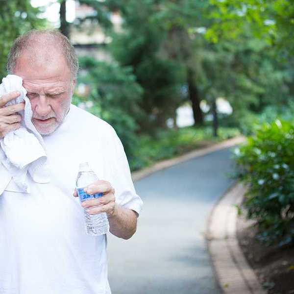 Closeup portrait old gentleman in white shirt having difficulties with extreme heat high temperature wiping sweat from face very tired isolated green trees paved road background