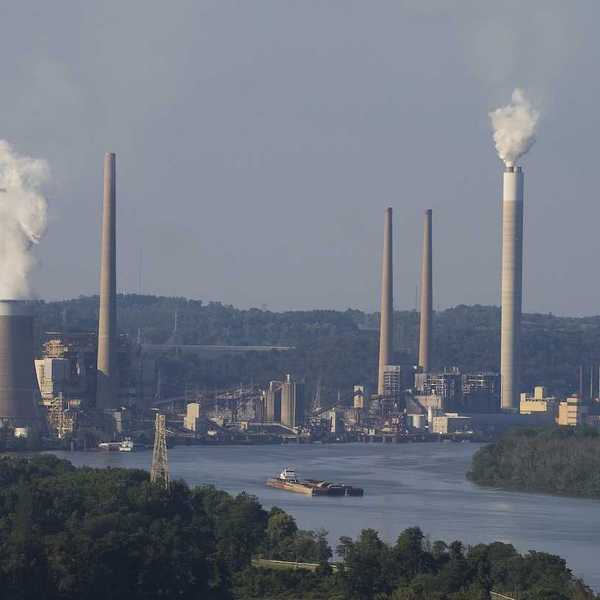 Coal fired electricity power plant along a river with a barge loaded with coal in the foreground.