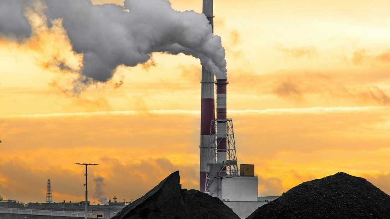 Coal fired power plant with two red/white smokestacks rising above a huge pile of coal, awaiting burning