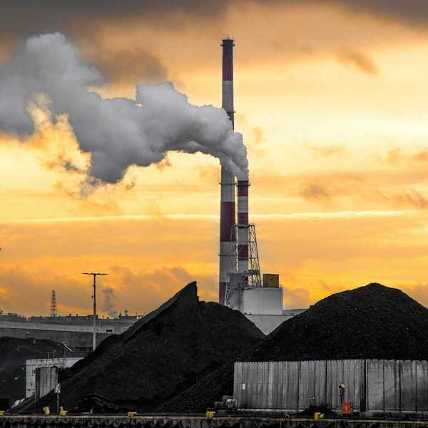Coal fired power plant with two red/white smokestacks rising above a huge pile of coal, awaiting burning