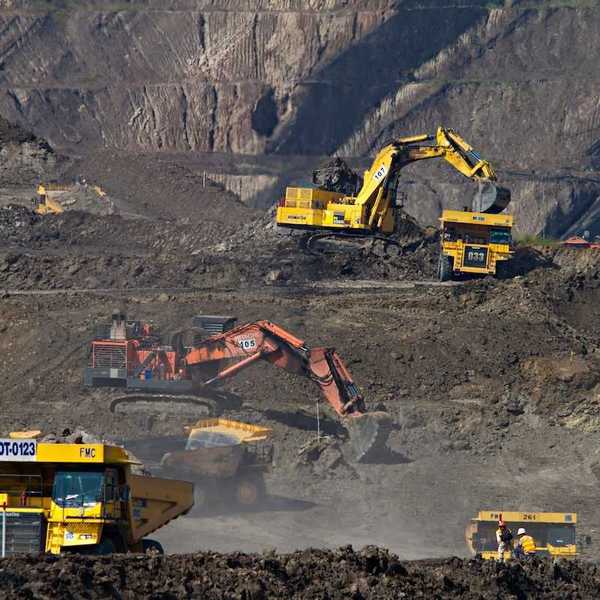 Coal mining operation featuring yellow rock trucks and excavators as well as one orange excavator in the center.