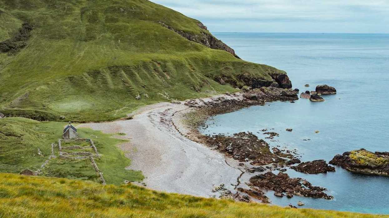 Coast of Scotland, Isle Of Rum. Long shot of green hills, isolated beach, stone structure.