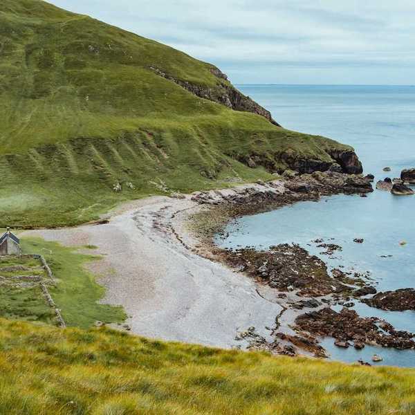 Coast of Scotland, Isle Of Rum. Long shot of green hills, isolated beach, stone structure.