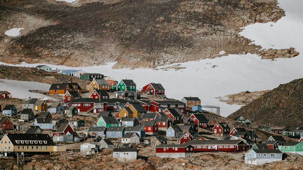Colorful houses on a rocky hillside with patches of snow in background.
