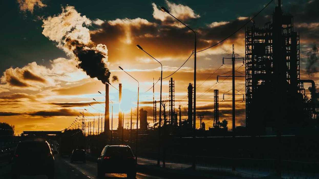 Commuters on an urban expressway beneath belching smokestacks.