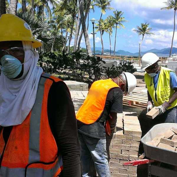 Construction workers move bricks on a tropical beach shoreline job site.