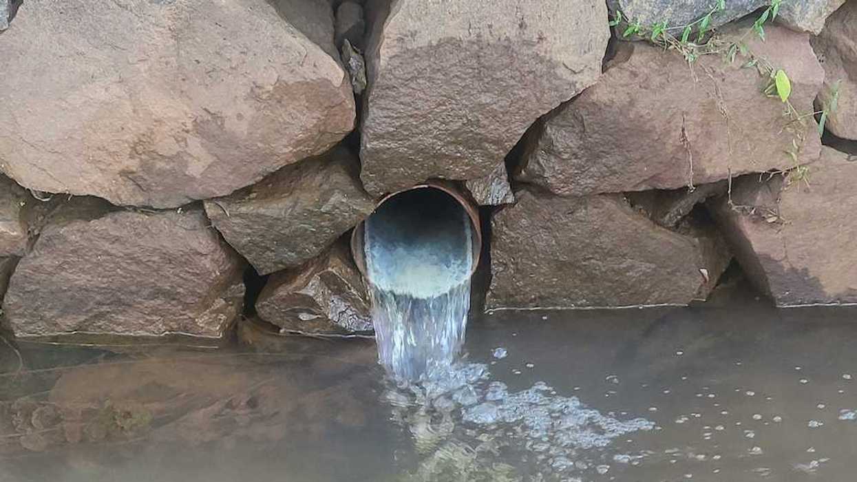 Culvert protruding from a stacked rock wall and discharging into a waterway