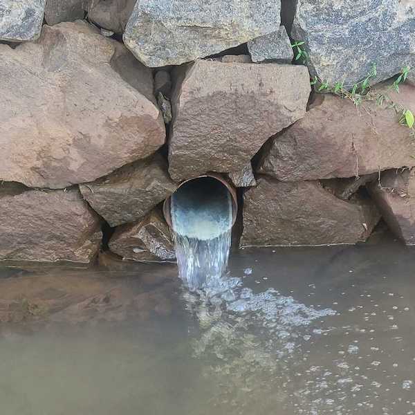 Culvert protruding from a stacked rock wall and discharging into a waterway