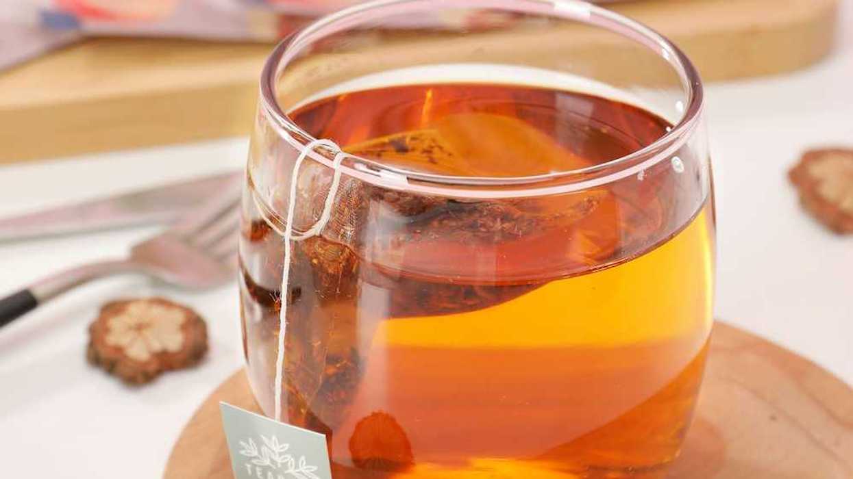 Cup of orange-colored tea with tea bag steeping in a clear glass cup