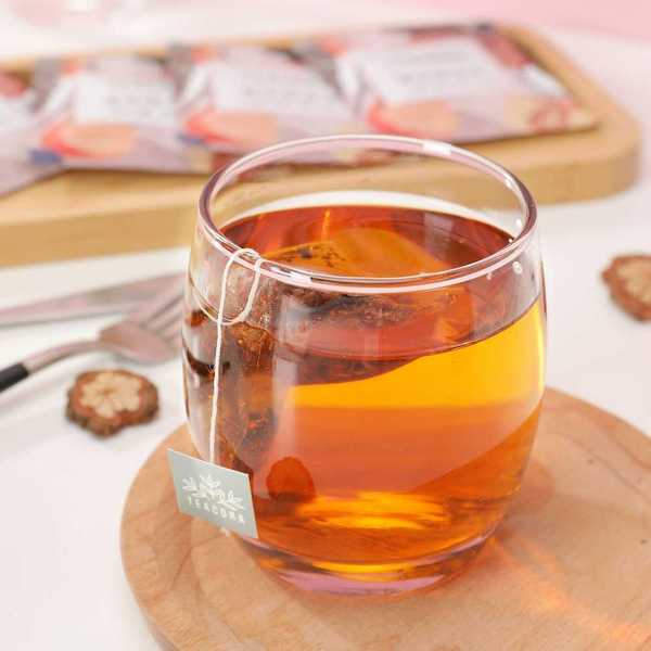 Cup of orange-colored tea with tea bag steeping in a clear glass cup