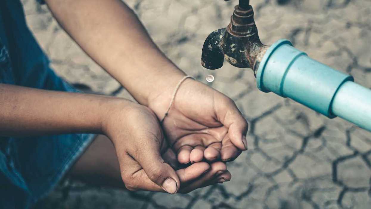 Cupped child-hands catching drops of water from a tap above cracked, dry earth