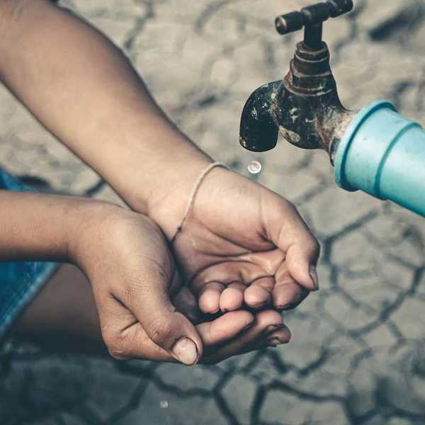 Cupped child-hands catching drops of water from a tap above cracked, dry earth