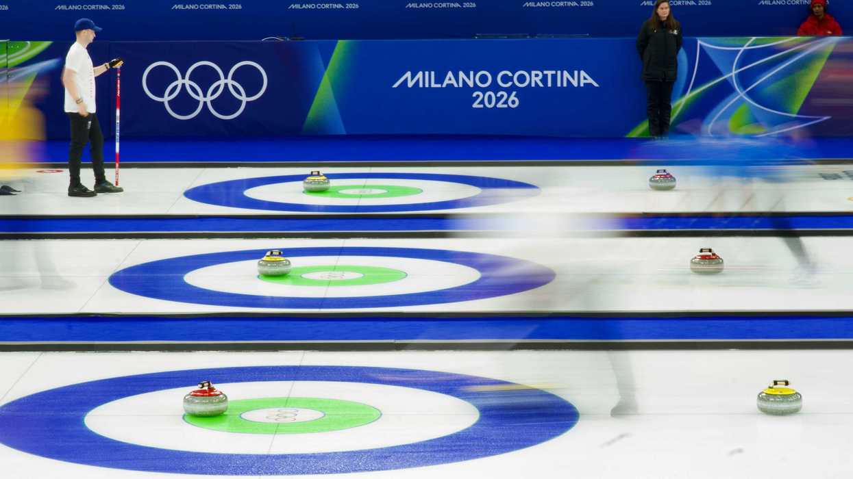 Curling match at Cortina Winter Olympics 2026 with athletes sliding stones on ice and fans in stands behind.