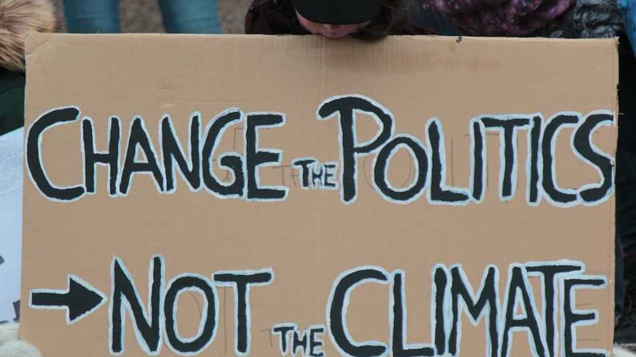 Demonstrator holding a sign reading "CHANGE THE POLITICS, NOT THE CLIMATE"